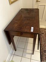 Side view of wooden drop leaf table showing one leaf extended and visible damaged knob.