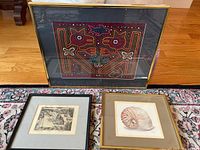Top view of all three framed artworks: colorful Mola textile, nautilus shell picture, and black and white street scene picture.