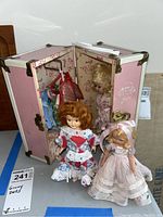 Three Ginny dolls, two standing in front and one visible inside open pink trunk, showing some wear and vintage clothing.