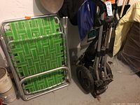 Photo showing two green and white woven folding lawn chairs with aluminum frames leaning against a wall beside the golf cart.