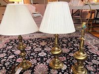 Three brass lamps on a carpet, two with shades, one without.