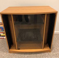 Front view of glass door media cabinet showing wooden frame, glass door, and black side accents.
