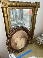 Rectangular gold frame mirror with ornate details, visible wear and chips on finish. The mirror is shown standing upright on a surface with some surrounding dishes visible.