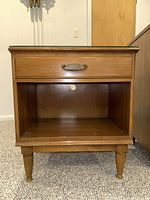 Front view of the wood nightstand showing the drawer with metal handle and open bottom shelf.