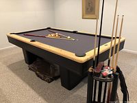 Angled view of full table showing rails, base, folded cover underneath and cue stand with cues