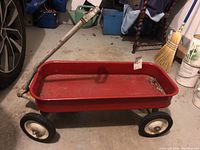 Full view of vintage red metal wagon with rust and metal handle.