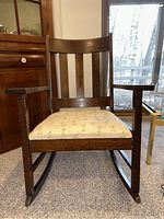 Front view of the wooden rocking chair showing the slatted back and upholstered seat.