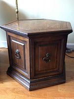 Front and side angle showing hexagonal shape, cabinet doors with metal ring handles, stepped base, and surface wear.