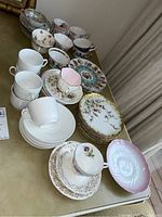 Overview of the various china dishes and teacups arranged on a surface showing multiple sets and patterns.