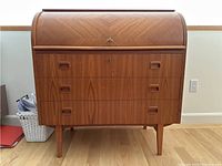 Front view showing tambour cover, three drawers with recessed handles, and legs