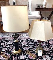 Two vintage lamps placed on a floral patterned rug. Left lamp has a black and brass base with a large white drum shade. Right lamp has a brass base with a cream rectangular shade.