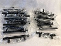Photo showing two groups of black metal drawer pulls individually wrapped in plastic. One group contains larger pulls and the other smaller pulls, along with mounting hardware.