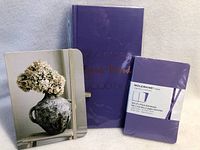Three new notebooks: one large purple hardcover with embossed text, one sealed Moleskine purple notebook set, and one small floral cover notebook.