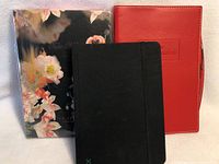 Three notebooks, floral cover, red cover with embossed text, black cover with elastic band