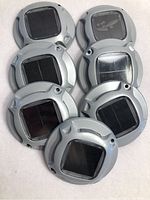 Seven gray plastic solar lights arranged showing the front solar panel sections with minor surface scuffs visible, capturing the overall lot.