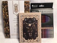 Three sketchbooks, two with floral covers and one with an artistic bull illustration, along with a set of 18 metallic colored pencils in a black box.