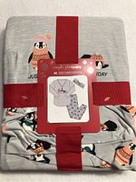 Folded pajama set with red ribbon packaging, showing top penguin graphic and pants with penguin print.