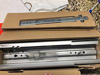 Box containing silver full extension drawer slides with mounting holes and installation accessories inside a plastic bag.