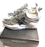 Side view of shiny silver Kenneth Cole women's Maddox jogger sneakers on top of the black Kenneth Cole New York box.