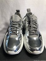 Front view of silver Kenneth Cole sneakers showing the shiny metallic finish, grey laces, and white soles.