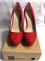 Front view of new red high heel shoes on their box, showing rounded toes and light interior lining.