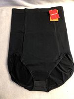 Front view of the black high-waisted brief shapewear showing tags and overall condition, laid flat on a surface.
