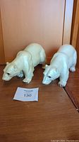 Photo showing two large white ceramic polar bear figures on a wooden surface, positioned side by side.