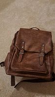 Overall closed view of the brown faux leather day pack backpack showing the flap with two buckled straps