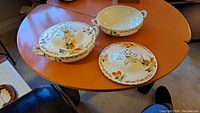 Photo of three floral serving dishes including one covered and two uncovered with lids on wooden table