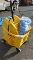 Yellow Brute mop bucket with wheels and yellow wringer, plastic packaging with blue mop head inside, mop handle visible.
