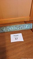 Photo of the brass 'NO SMOKING PLEASE' sign placed upright on a wooden surface, showing full text and sign dimensions.