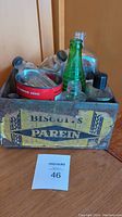 Photo showing several old glass bottles placed inside a metal tin box labeled 'Biscuits Parein'