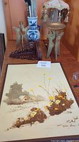 Photo showing original painting, brass fans, ceramic vase, wooden shelf, and lamp on a wooden surface