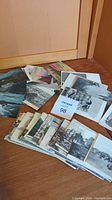 Several dozen assorted early 1900s postcards laid out on floor, mostly black and white and sepia tone with scenic and figurative images.