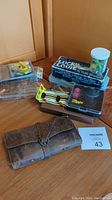 Overall fishing tackle assortment with leather fly wallet, wooden lure case, original Lucky Louie Plugs box, Mepos plastic case, and small container of accessories.