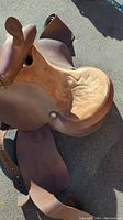 Front angled view showing saddle seat with embossed design, saddle horn, leather skirts, and stirrups.