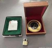 Two Ronson lighters and a brass compass in wooden box shown together on gray table surface.