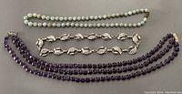 Three necklaces laid flat showing amethyst beads, silver leaf motif necklace, and green stone necklace