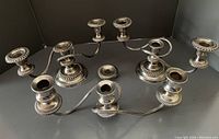 Two silver-plated candelabra with multiple arms and bases arranged in a complex configuration on black background.