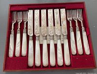 Complete set of 12 pieces displayed in red felt-lined case, including 6 knives and 6 forks with mother of pearl handles and silver-plated parts.