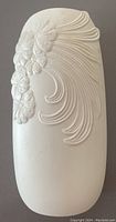 Front view of white bisque vase showing prominent floral and swirl relief design.