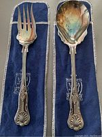 Top view of vintage Silver Gifts serving fork and spoon set on blue fabric pouch, showing ornate handle detailing