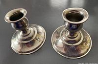 Two sterling silver candlesticks shown from top angle on black surface, showing tarnish and bent top on one.