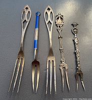 Top view of 5 sterling silver pickle forks showing varied ornate handles and tines