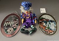 Photo showing two oval faux stained glass window hangers and one seated clown figurine on a flat surface
