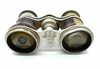 Front view of antique opera glasses showing metal body and Mother of Pearl decoration with engraving dated 1886