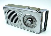 Front and side view of the vintage 1950s Oldsmobile Trans-Portable radio showing its chrome metal case, speaker grille, tuning dial, and handle.