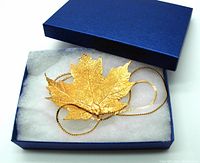 Maple leaf pendant arranged in blue cushioned gift box with chain loosely coiled