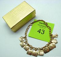 Gold plated Ten Commandments charm bracelet displayed with its textured light gold colored gift box.