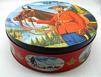 Angle view of round tin showing detailed Mountie on horseback graphic on lid and multiple smaller Mountie patrol scenes around the tin sides with red background and maple leaf accents.